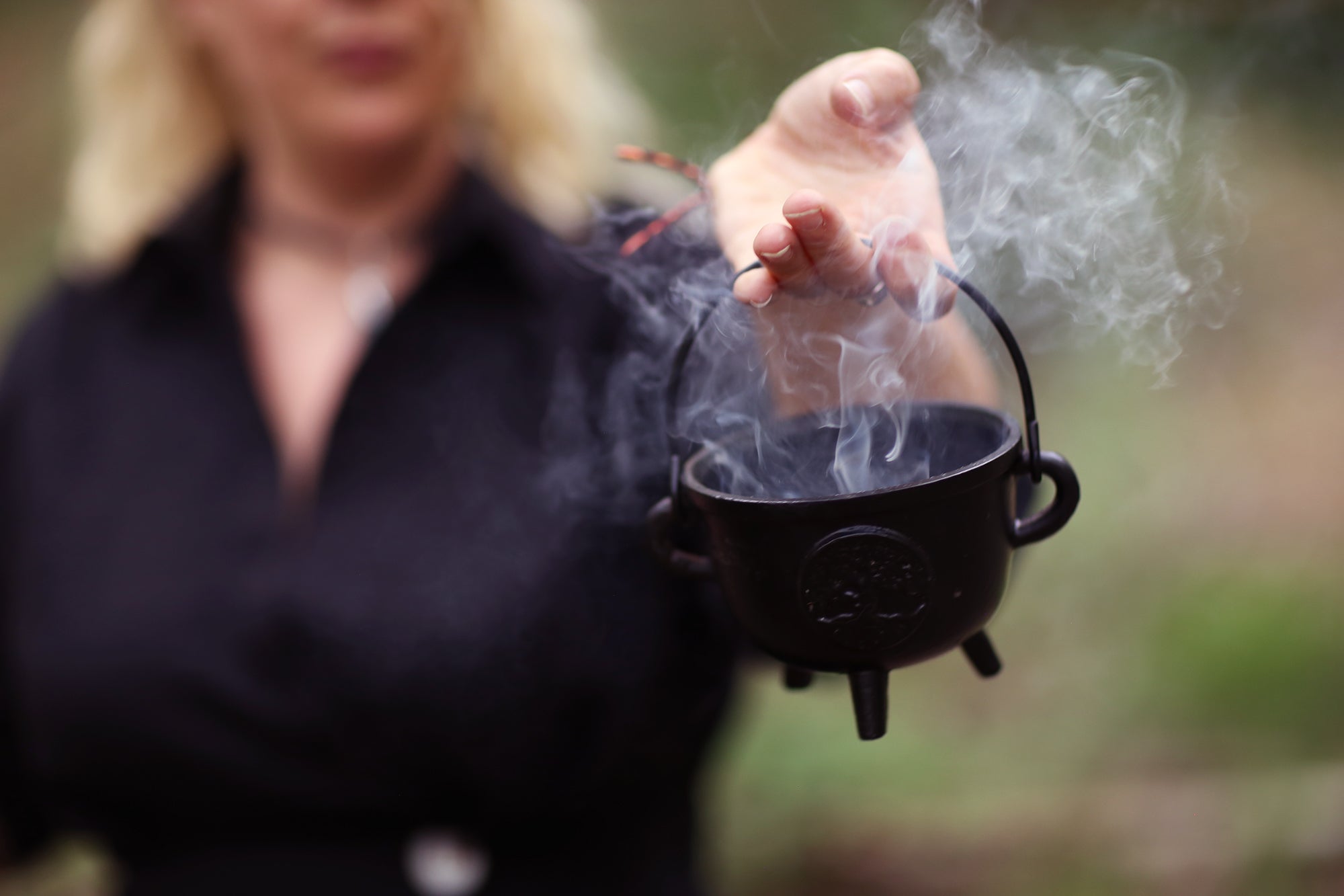 Person holding a black cauldron with smoke coming out against a blurred background